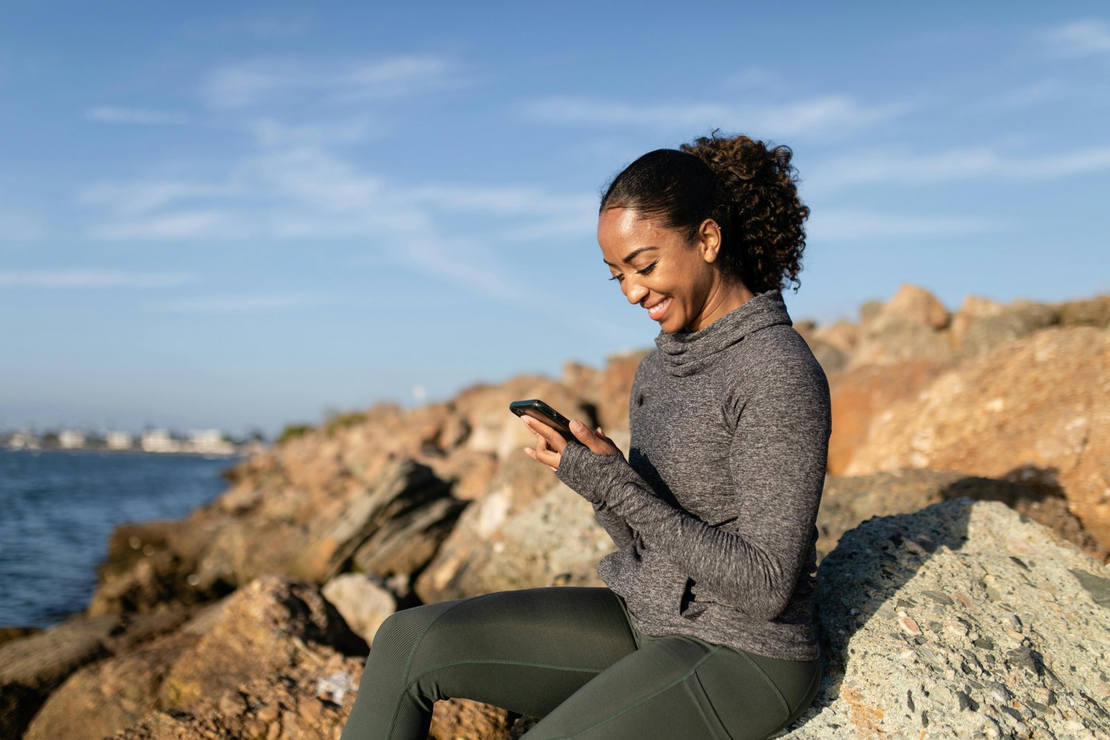 A woman sitting on a rock, looking at her mobile phone
