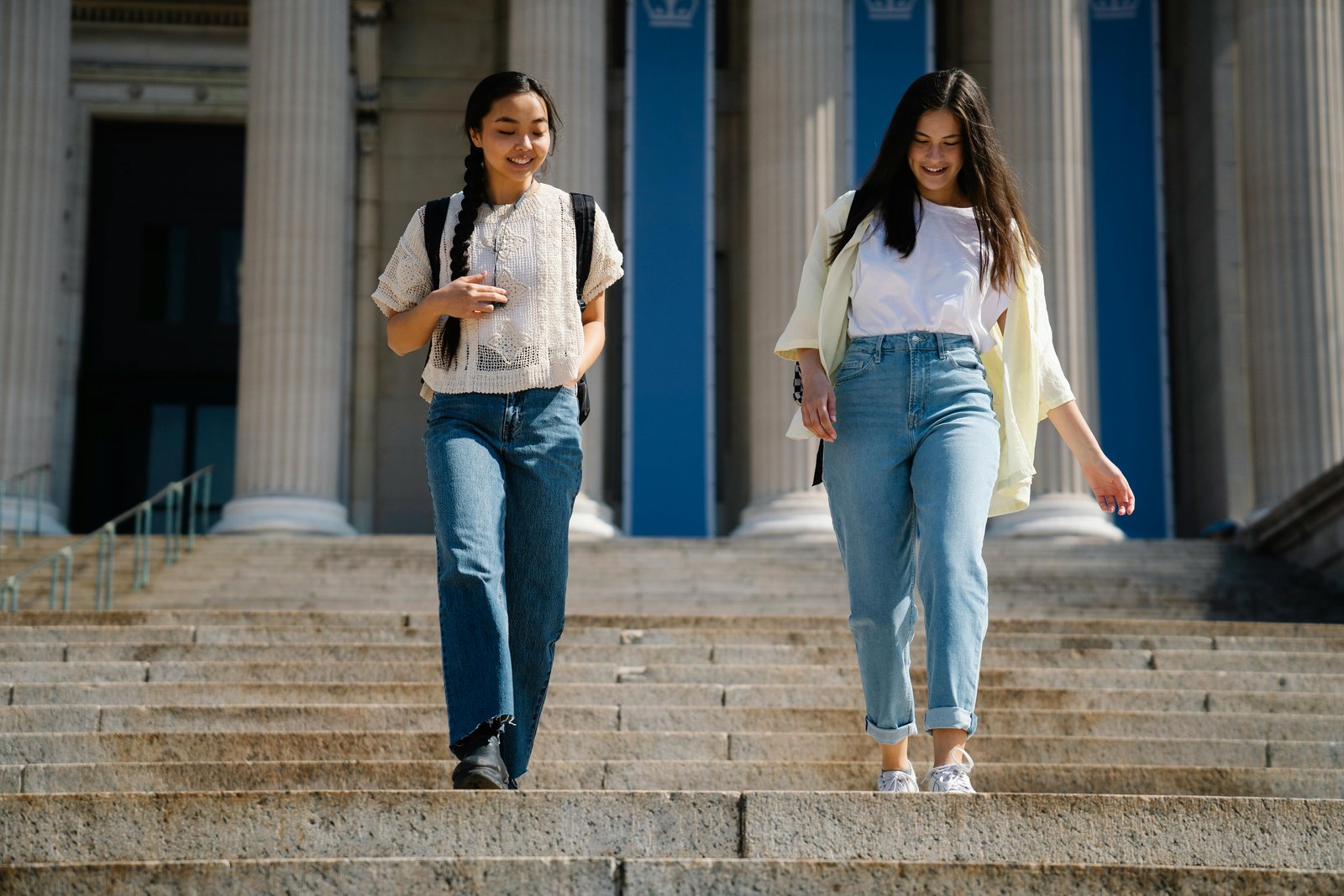 Two young women walking down some steps, smiling and chatting to one another casually